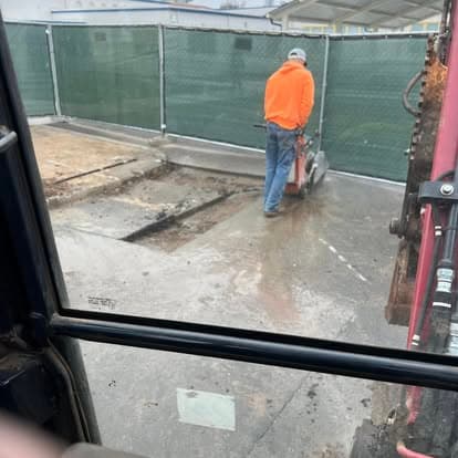 Worker operating a concrete saw on a construction site with green fencing in the background.