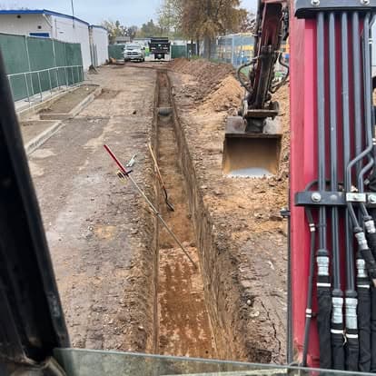 Excavation trench for utility installation with construction equipment nearby.