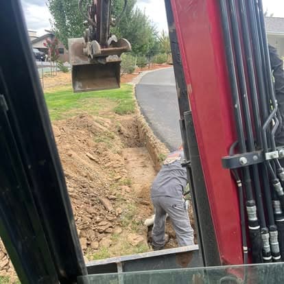 Excavator digging a trench with a worker on a residential property.