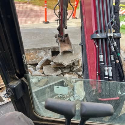 Excavator digging through concrete at a construction site, showcasing heavy machinery in action.
