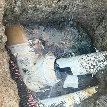Leaking broken pipe surrounded by dirt, with water gushing from the damaged section.