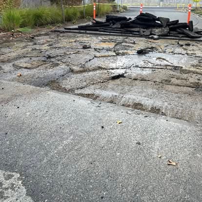 Damaged road surface with debris and construction signs indicating repairs needed.