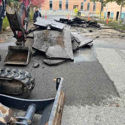 Construction site with heavy machinery removing asphalt from a damaged road.