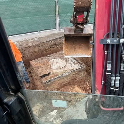 Excavation site with a worker and heavy machinery revealing a buried structure.