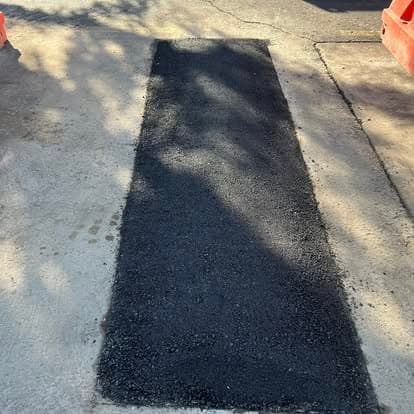 Freshly laid black asphalt patch on a roadway with construction barriers.